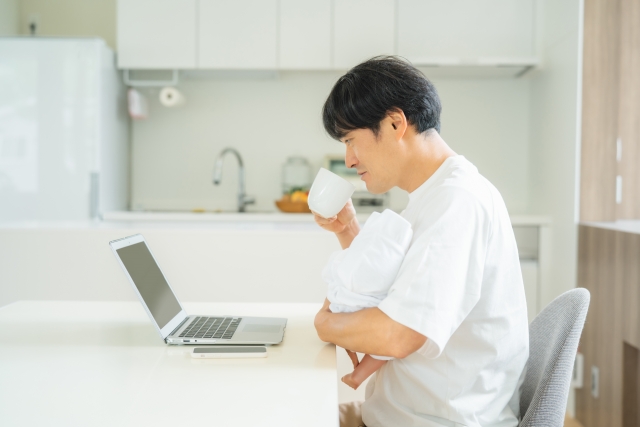 赤ちゃんと抱っこしながらコーヒーを飲んでパソコンを見てる男性