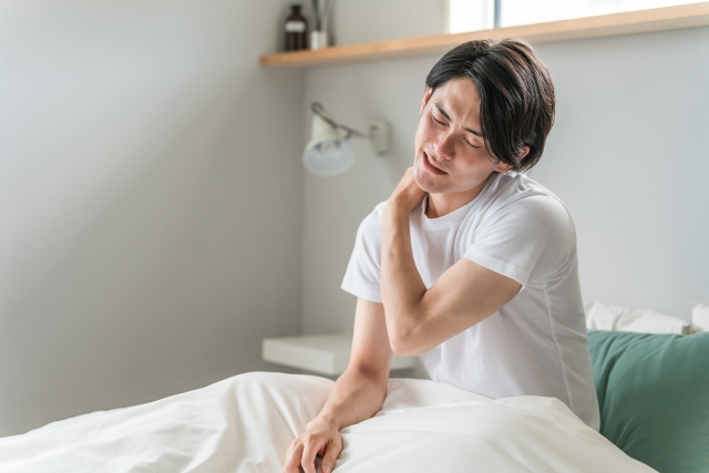 寝違えてベットで肩を触る男性