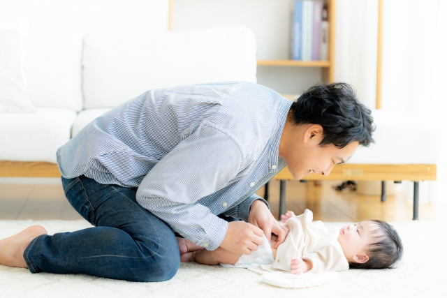 赤ちゃんの顔を見ながらおむつを変えるパパ